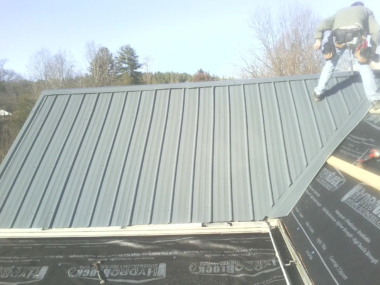 Crew installing dark green standing seam panels over synthetic underlayment in Lilliwaup