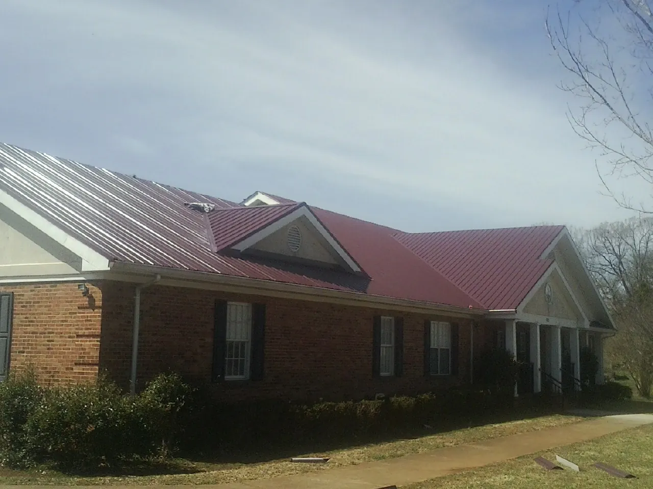 Red metal roof with gabled entries on a long brick building, from a Hail Damage Roof Repair job in Lilliwaup