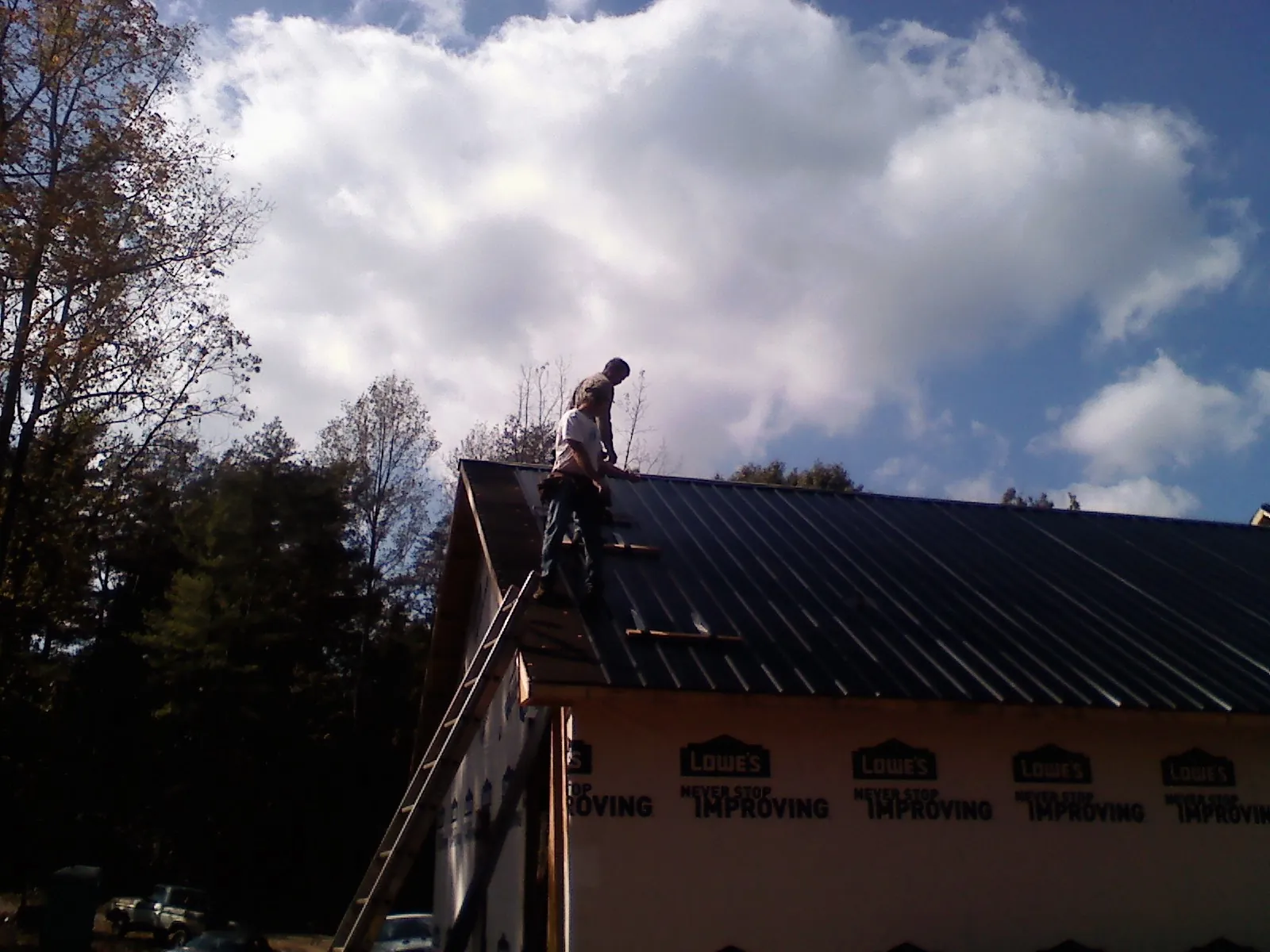 Roofer fastening dark metal panels high against a cloudy sky, from a Roof Inspection job in Lilliwaup