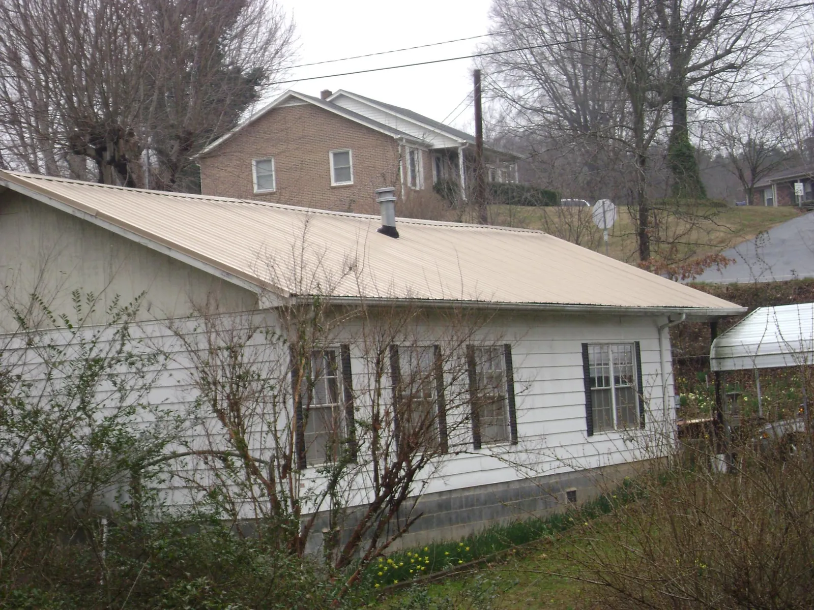 Tan metal roof on a white sided house set into a hillside — Commercial Roofing by Roofing Brothers in Lilliwaup